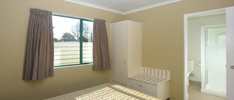 A bedroom with a bed, a wardrobe, a window with curtains, and a door leading to a bathroom.
