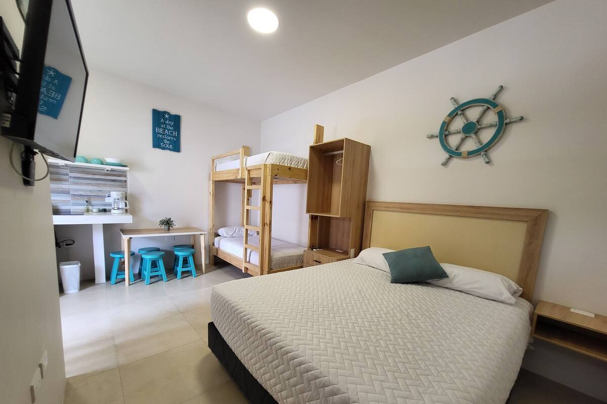 A room with bunk beds, a desk with stools, a ship's wheel decoration, and a sign on the wall.