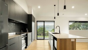 A modern kitchen with dark cabinets, a wooden countertop island, and a large window offering a view of the outdoors. - Fiddle View | Alfresco Dining with Mountain Views (Tawonga South)