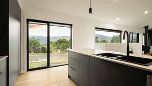 A modern kitchen with a large island, dark cabinetry, and a view of the outdoors. - Fiddle View | Alfresco Dining with Mountain Views (Tawonga South)
