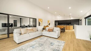 A modern living room with a sectional sofa, a dining area, and a kitchen with dark cabinets and pendant lighting. - Fiddle View | Alfresco Dining with Mountain Views (Tawonga South)