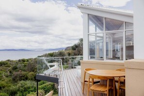 Ein moderner Balkon mit Holztisch und -stühlen, der einen schönen Panoramablick auf Meer und Hügellandschaft bietet.
