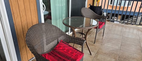 A balcony with wicker furniture, a glass table, and a view of the outside.