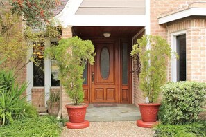 A brick house with a wooden front door, two potted plants, and a small garden area. - Beautiful Three Bedroom Home with Scenic Backyard (Houston)