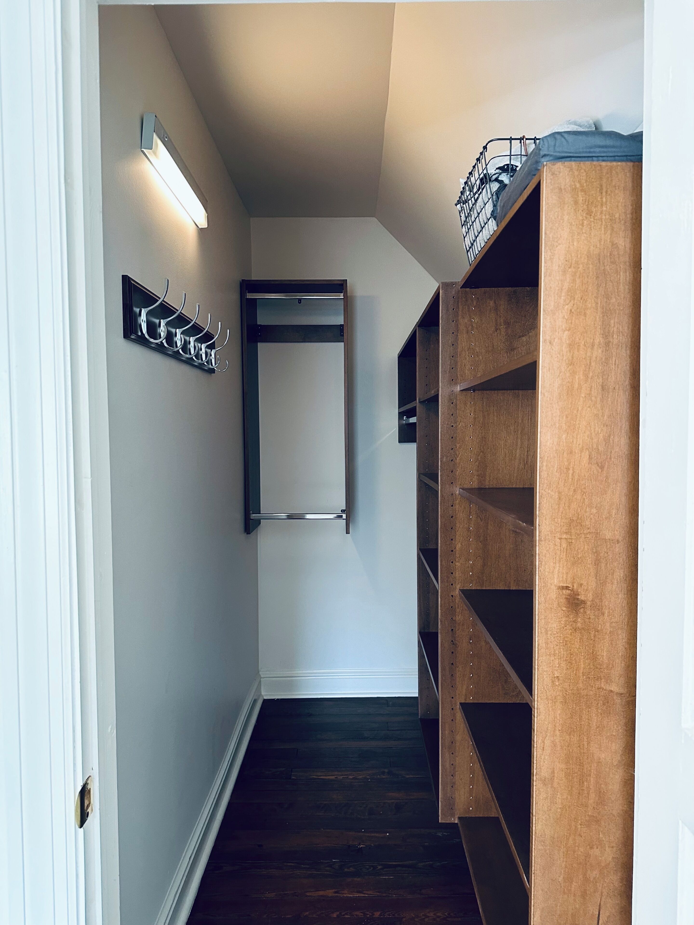 Un couloir étroit, avec une étagère en bois sur le côté droit, un porte-manteau sur le côté gauche et une porte au fond.