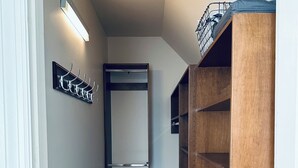 A narrow hallway with a wooden shelving unit on the right, a coat rack on the left, and a door at the end. - Cozy Mother-In-Law Suite (Pittsburgh)