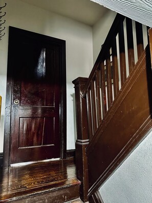 Un escalier en bois avec une rampe et une porte en bois foncé dotée d’un panneau de verre.