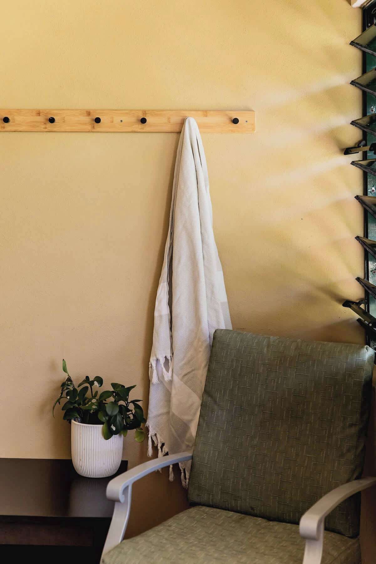Een hoek van een kamer met een houten plank, een potplant, een stoel en een handdoek die aan de muur hangt.