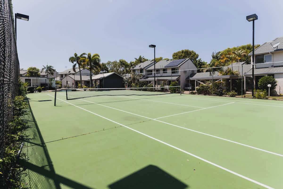 A tennis court with a net, surrounded by houses and palm trees.