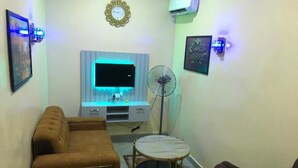 A living room with a sofa, a small round table, a TV, and a fan.