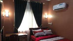 A bedroom with a bed, a desk, and an air conditioning unit.