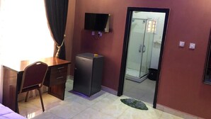 A hotel room with a desk, chair, TV, and a door leading to a shower area.
