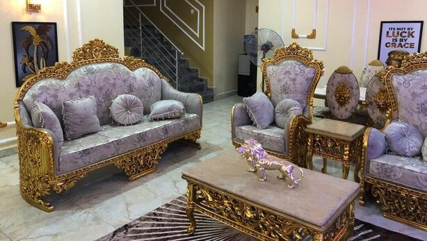 A luxurious living room with ornate furniture, a staircase, and a decorative mirror.