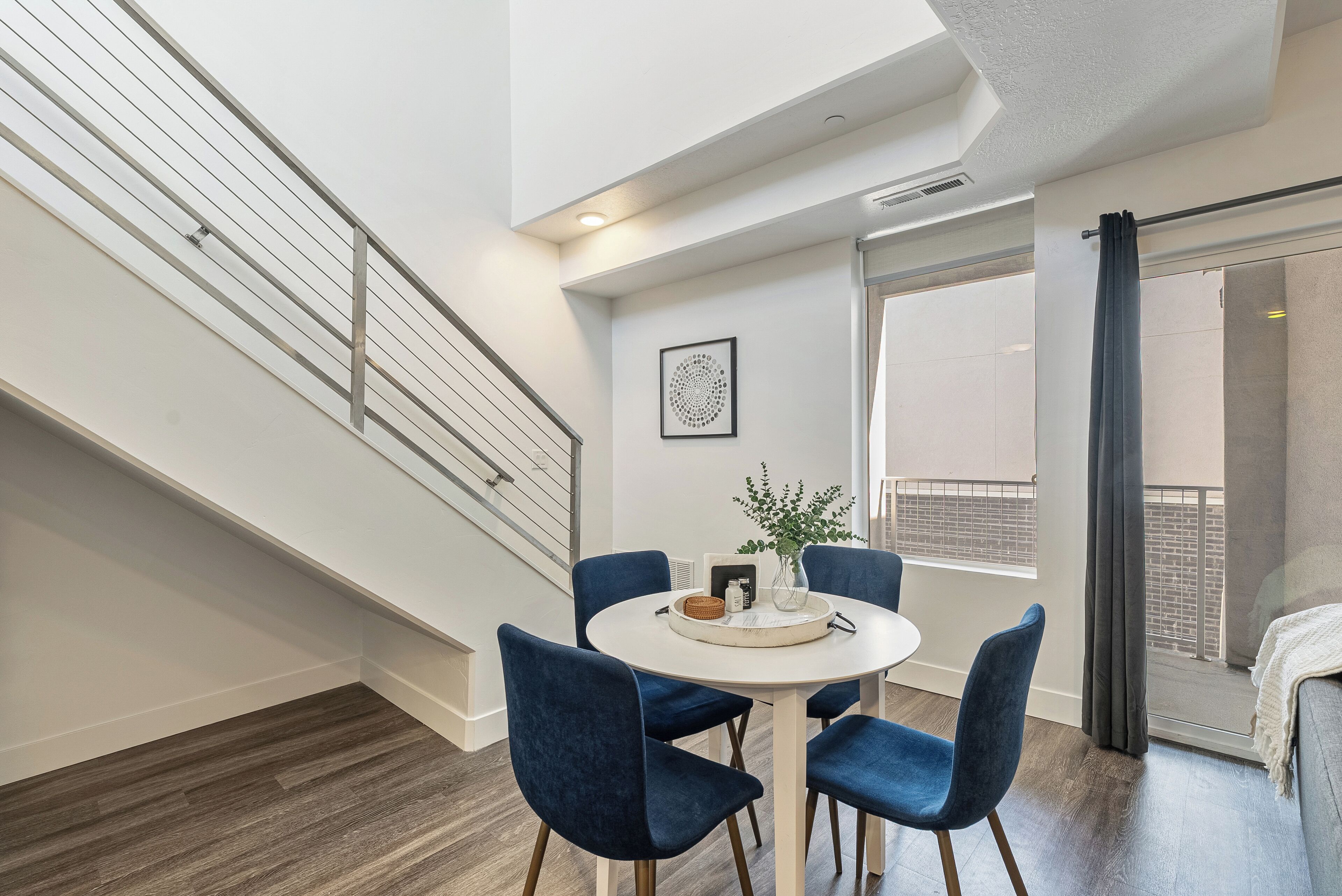 Un espace repas moderne avec une table ronde, quatre chaises bleues et un vase agrémenté de plantes vertes.