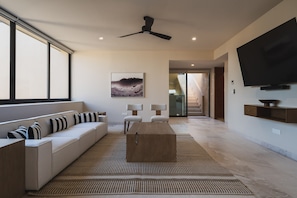 Una sala de estar moderna con sofá, una mesa de centro, ventilador de techo, televisor de pantalla plana y un amplio ventanal.