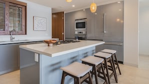 A modern kitchen with a central island, bar stools, stainless steel appliances, and pendant lighting. - Penthouse Arenamar in Punta Mita (Punta de Mita)
