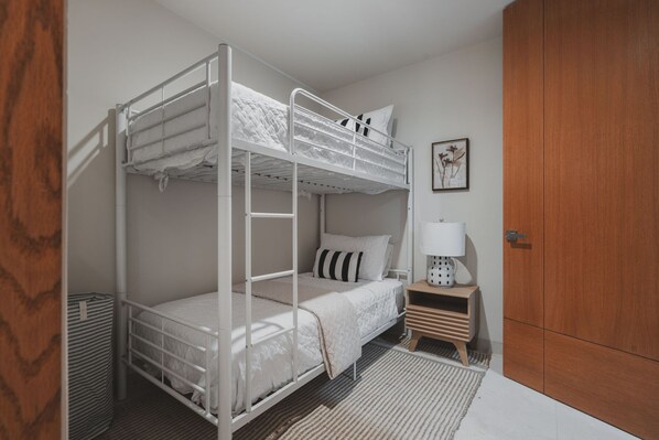 A bunk bed room with a wooden wardrobe, a small bedside table with a lamp, and a framed picture on the wall. - Penthouse Arenamar in Punta Mita (Punta de Mita)