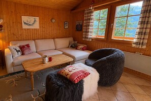 Ein gemütliches Zimmer mit Holzvertäfelung, einer Couch, einem Couchtisch, einem Sessel und einem Fenster mit Vorhängen.