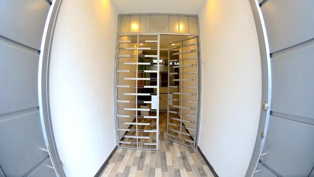 Un couloir étroit doté d’une porte moderne aux lignes courbes, ornée d’un motif en treillis métallique.