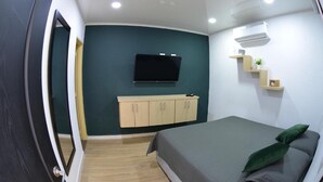 A bedroom with a bed, a TV mounted on the wall, a wooden cabinet below the TV, and a small shelf with a plant. - hotel la hermosa (Guadalajara de Buga)