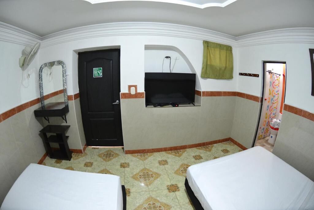 A hotel room with two beds, a black door, a small sink, a mirror, and a window with a curtain.