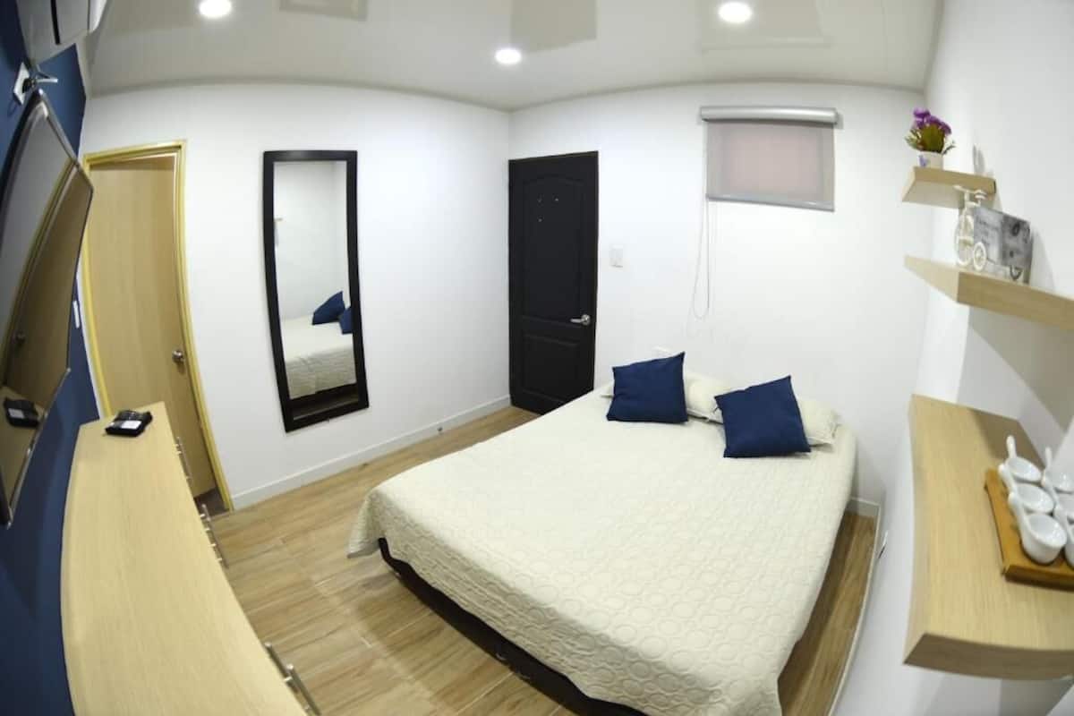 Une chambre à coucher comprenant un lit, un miroir, une porte et une étagère ornée d’objets décoratifs.