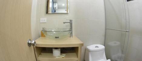 A compact bathroom with a glass bowl sink, a toilet, and a shower enclosure.