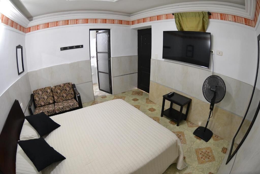 Una habitación de hotel con una cama, una silla, un televisor y un ventilador.
