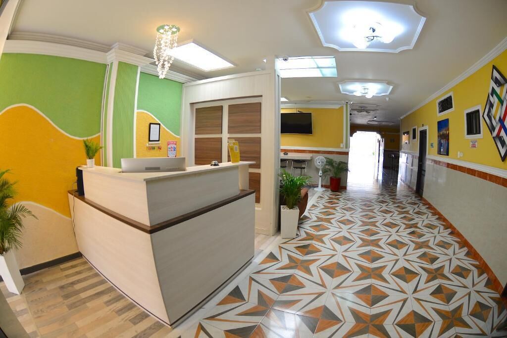 Vestíbulo de hotel con mostrador de recepción, suelo estampado y pared verde.