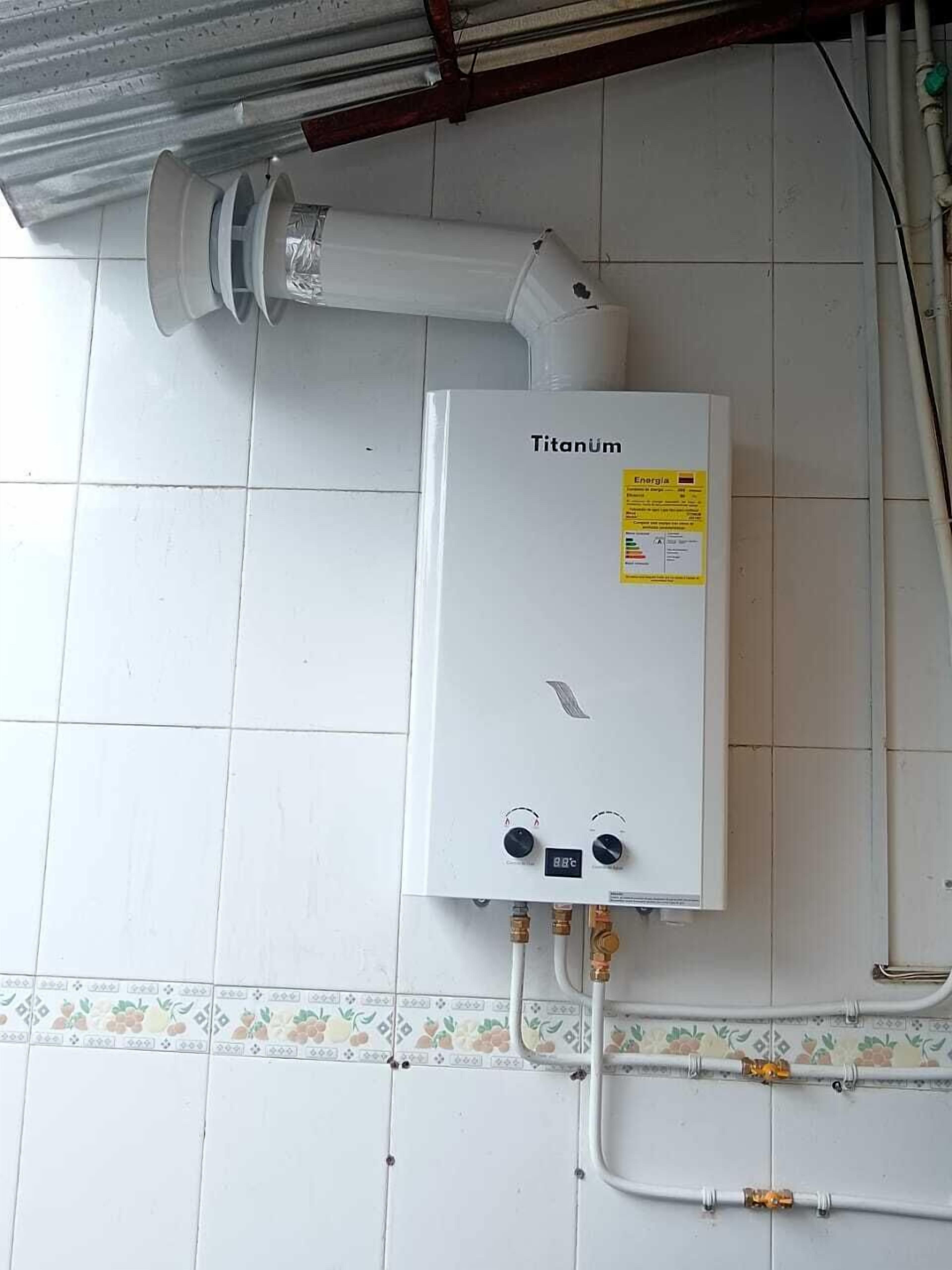 Ein weißer Warmwasserbereiter mit dem Aufdruck 'Titanum', zwei Drehreglern und einer digitalen Anzeige, verbunden mit einem gefliesten Boden mit dekorativer Bordüre.