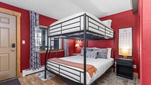 Een slaapkamer met een stapelbed, een rode muur, een kamerbreed tapijt met patroon, een bedlampje en een ingelijst beeld aan de muur.