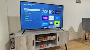 A flat-screen TV on a wooden TV stand with a shelf below displaying board games. - 12th Floor Studio at Downtown.  Parking Included (Edmonton)
