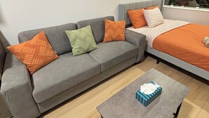 A modern living room with a grey sofa, orange and green cushions, a grey coffee table, and a framed plant on the wall. - 12th Floor Studio at Downtown.  Parking Included (Edmonton)