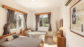 Ein Schlafzimmer mit zwei Betten, einem kleinen Schreibtisch, einem Stuhl, einem Heizkörper und einem Fenster mit Vorhängen.