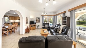 Ein modernes Wohnzimmer mit einer schwarzen Ledersofa, einem Holztisch und einem Fernseher. Es gibt eine Essecke mit Holzkästen und einem Tisch, sowie eine Küche mit Holzschränken und einem Fernseher.