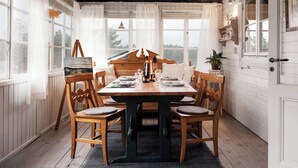 Un coin repas avec une table et des chaises en bois, un tableau au mur et de grandes fenêtres avec des rideaux.