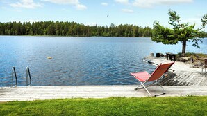 Une terrasse au bord du lac avec une chaise rouge, une jetée en bois et un arbre.