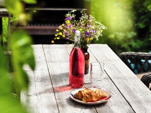 Een houten tafel met een fles rode vloeistof, een glas en een bord met gebak.