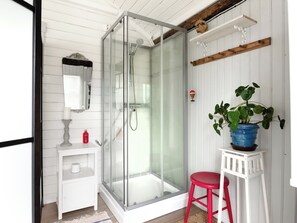 Een douche met glazen wanden, een wit wastafelmeubel en een rode kruk.
