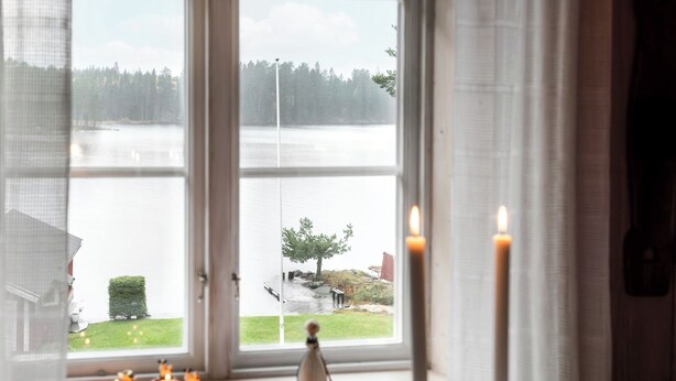 Une pièce dotée d’une grande fenêtre donnant sur un lac, d’une table en bois ornée de bougies et d’un intérieur rustique.