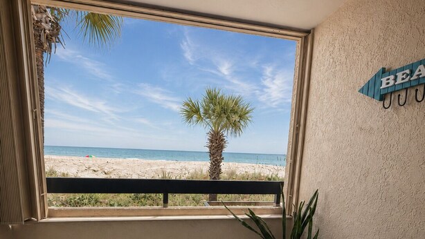 A balcony with a view of the beach, a palm tree, and a sign that reads 'BEACH.' - Oceanfront Getaway with Stunning Views , Pool, & Easy Beach Access (North Myrtle Beach)