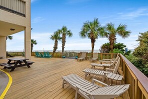 A wooden deck with lounge chairs and a picnic table, overlooking the ocean with palm trees. - Oceanfront Getaway with Stunning Views , Pool, & Easy Beach Access (North Myrtle Beach)