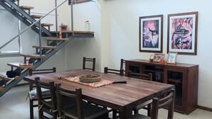 A dining area with a wooden table and chairs, a staircase, and two framed artworks on the wall. - Splendid house, very bright, 3 bedrooms, 3 bathrooms, kitchen, barbecue. Courtyard (Chascomús)