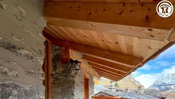 A wooden deck with a stone wall, a bench, and a red chair. - La Liete - 1st Floor (BESSANS)