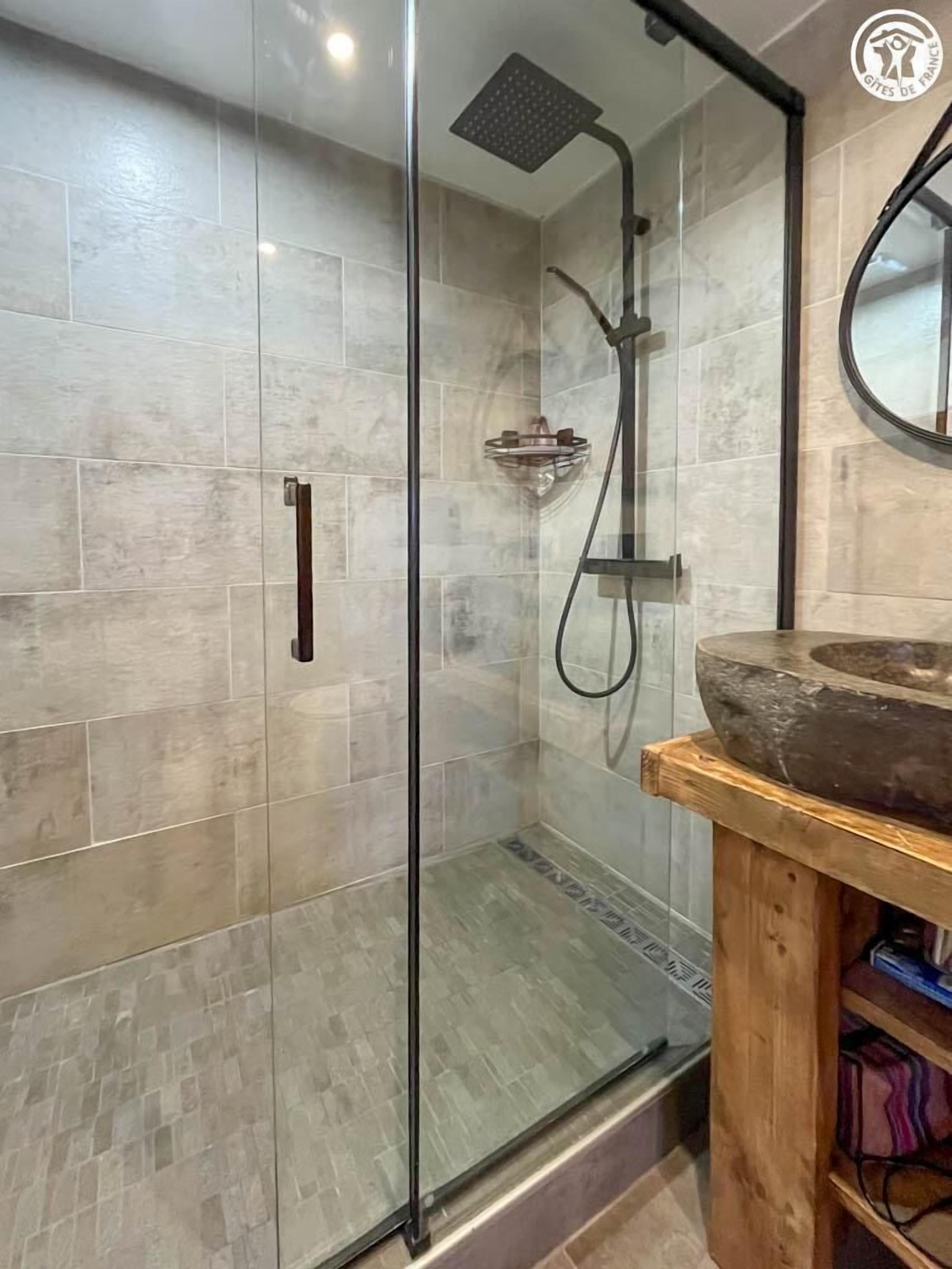Une salle de bain moderne dotée d’une douche à parois de verre, d’un meuble-lavabo en bois avec un grand vasque en pierre et d’un miroir au-dessus du meuble-lavabo.