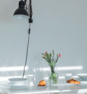 Ein Tisch mit einer klaren Glasvase, gefüllt mit rosa Blumen, einem Croissant und einer Tasse.