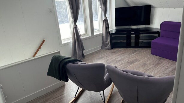 A modern living room with a flat-screen TV, a purple sofa, and a wooden floor.