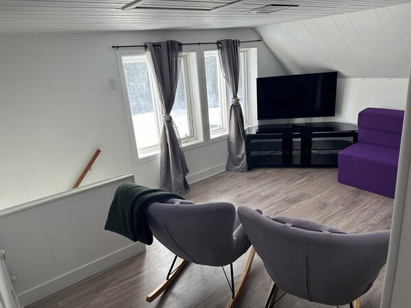 A modern living room with a flat-screen TV, a purple sofa, and a wooden floor.