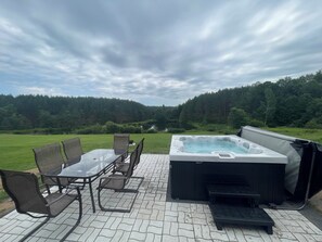 Eine Terrasse im Freien mit Whirlpool, Stühlen und Blick auf eine bewaldete Landschaft.