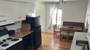 A modern kitchen with white cabinets, a black refrigerator, a stove, and a dining area with a wooden table and chairs.